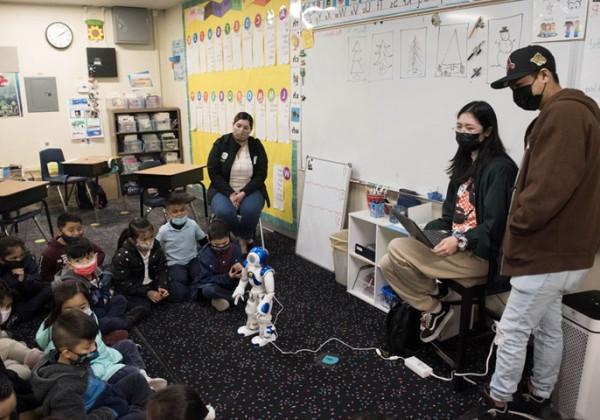 在教室里，一个小型人形机器人在学生面前表演.